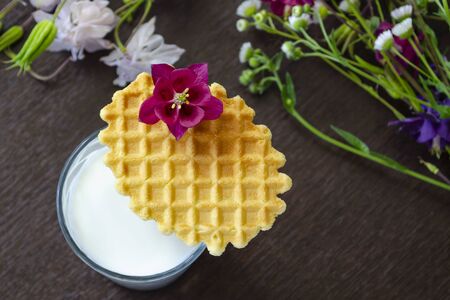 A glass of milk with a wafer and a flower. Selective focus