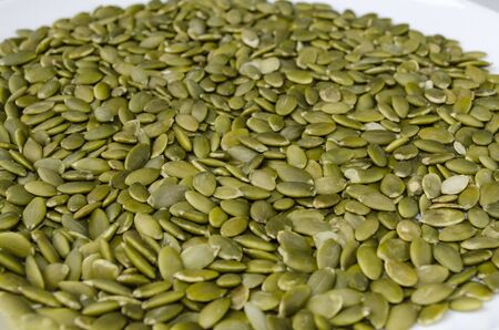 Peeled green pumpkin seeds sprinkled on a white plate. Selective focus.
