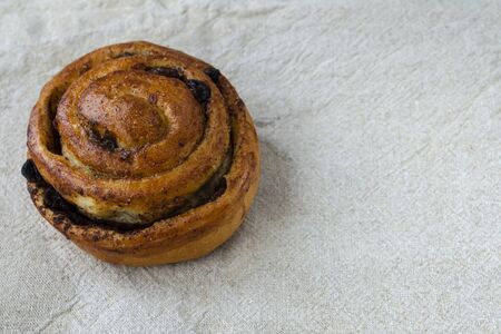 Bun with raisins and cinnamon on a linen tablecloth. Close-up.