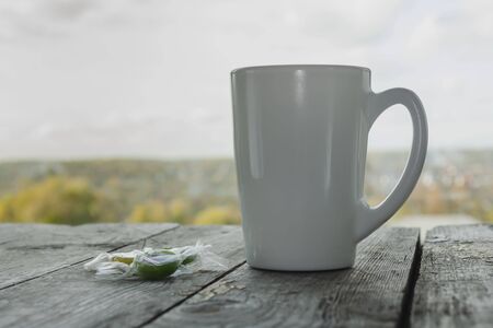 White mug and candies on a wooden table against the background of a window view on a high floor....