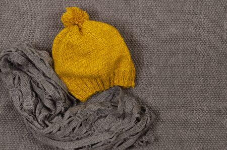 Yellow mustard beret with pampon and gray scarf on a gray knitted background