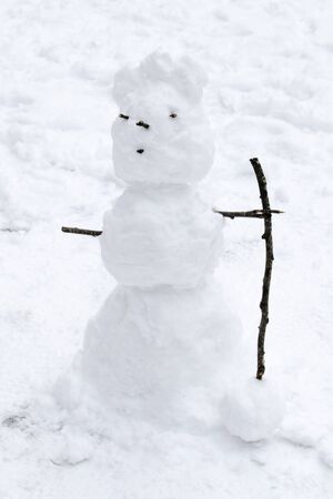 Snowman on the street with a cane from a tree branch, eyes and mouth made of sticksの写真素材