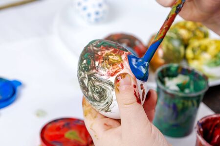 A child paints a white egg with a brush. Easter preparation