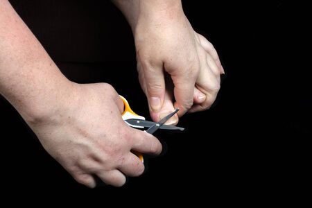 woman shears toenails with safe scissors on a dark black background