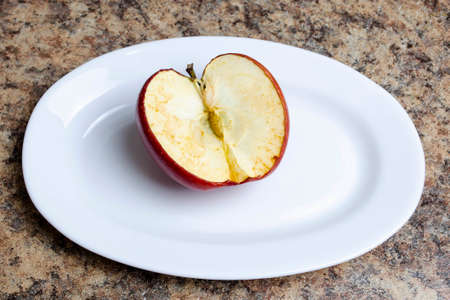 A cut red apple with a darkened and withered cut on a white plateの写真素材