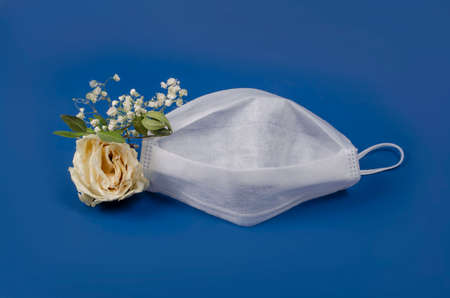 White medical mask and white dry flowers on a blue background. Concept symbol of death from infectious diseasesの写真素材