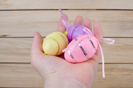 Multi-colored Easter eggs in a person's hand on a beige wooden backgroundの写真素材