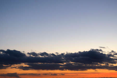 Bright orange sunset with clear sky above and dark clouds near the horizonの写真素材