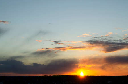 Bright sun at sunset in an orange blue sky with clouds. natural background.の写真素材