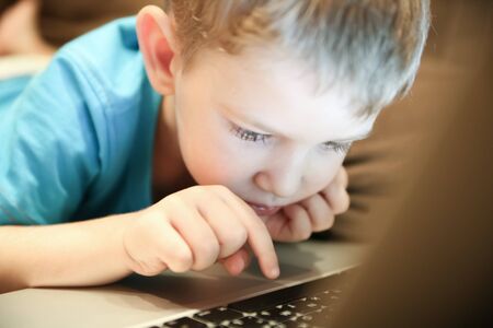 Little boy concentrates on working on the notebook lying on a sofaの写真素材
