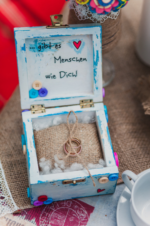 Rings in rustic wood box with buttons on a sackcloth. Felt wedding bouquet handmade in the glass twine. White tea set. Candles, cookies on suitcase and blanket.の写真素材