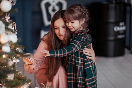 Happy little smiling girl with her mother near a christmas tree.の写真素材
