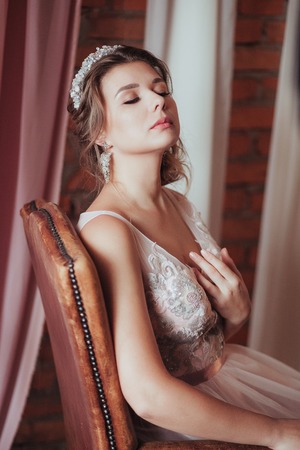 romantic Woman in pink bridal dress sitting on brown armchair. Face with closed eyes lifted up. Indoor, interior, studio.の写真素材