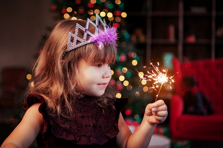 Happy small girl looking with admiration at burning sparkler in her hand over Christmas background.の写真素材