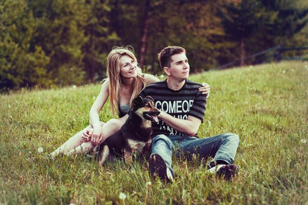 Couple with a dog sitting on the grass in the forestの写真素材