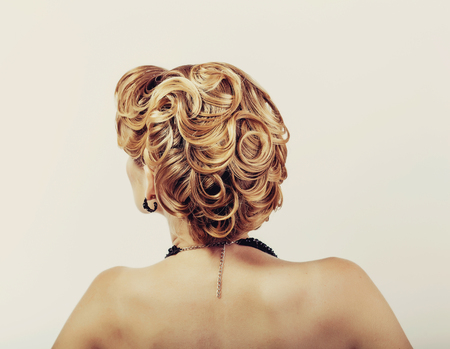 beautiful woman with blond hair wearing little black dress touching her neck view from the back on whiteの写真素材