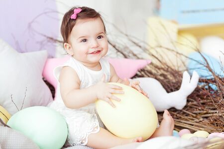 Happy baby girl in big Easter nest with eggs. Easter holiday concept: nest with baby hare