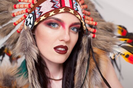 Indian woman with traditional make up and headdress looking at the camera. Redskin Indian woman on white background with a roach on her headの写真素材