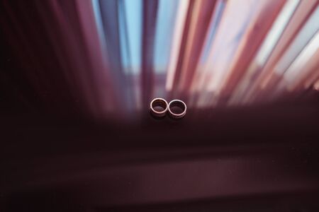 Two rings on wooden table with blurred curtains reflection.の写真素材