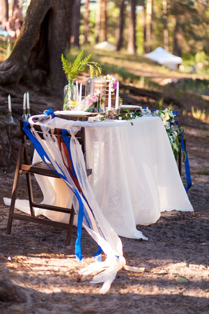 Wedding decorations. Wooden photo zone located in forest and decorated by table, chair, glass dome, ribbons and flowers.の写真素材