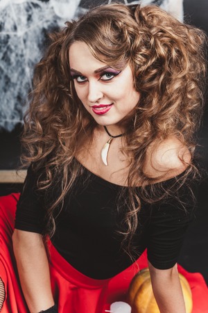 Halloween portrait of witch girl sitting on the floor with black wall and spider web on background. Wears a blouse and red skirt.の写真素材