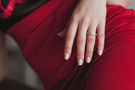 Close-up of tender ring on womans hand with white nails. Red dress, vertical shotの写真素材