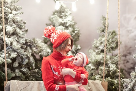 Happy family mother and child boy in santa hat near snow covered Christmas trees with sitting on...