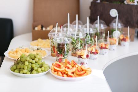Catering for wedding party. Plenty of mixed various kinds of sliced fruit, vegetables, cheese, salads in plastic cups on table indoorsの写真素材