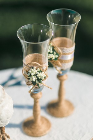 Two wedding champagne glasses decorated with twine and flowers standing on tableの写真素材