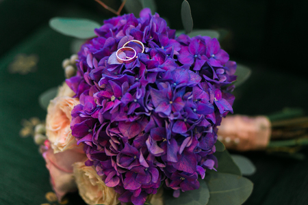 Golden wedding rings on bouquet of purple hydrangea, pink roses flowers with lilac ribbons in rustic style.の写真素材