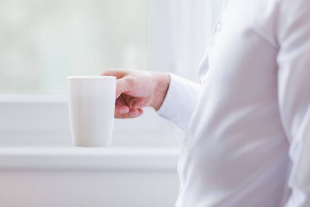 The groom or man holds a cup of coffee in hand. On white window backgroundの写真素材