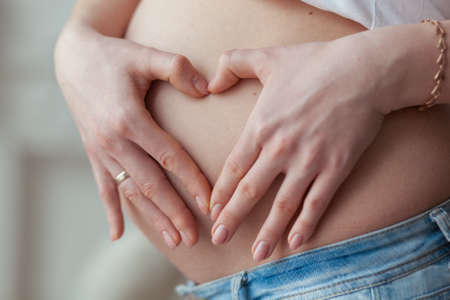 Pregnant woman making a heart shape with her hands over her tummyの写真素材