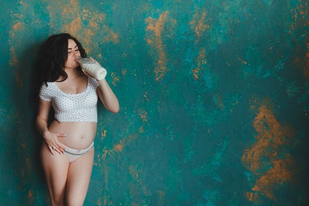 Pregnant woman drinking milk. Isolated on rustic wall backgroundの写真素材