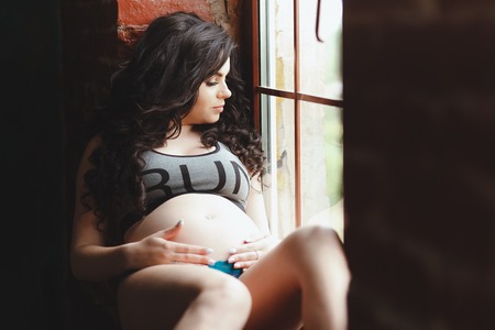 young pregnant woman sitting on the window sillの写真素材