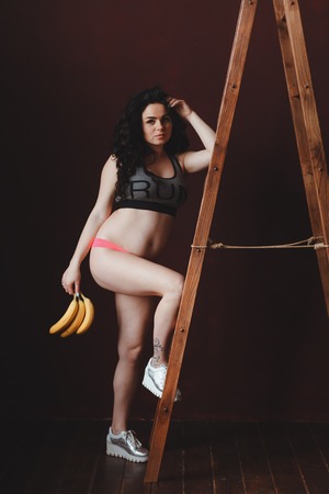 pregnant young woman fit looking, holding bananas at the ladder in loft studio