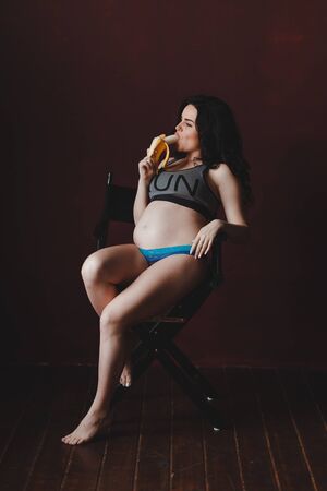 pregnant woman is sexually bites banana sitting on chair in loft studioの写真素材