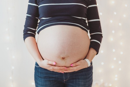 Close-up of pregnant womans big hairy belly on bright bokeh lights backgroundの写真素材