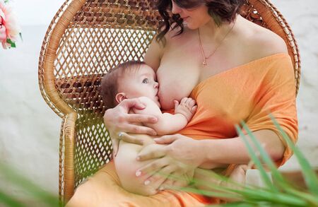 Mother breastfeeding her little baby girl in her arms sitting in wooden armchair. Close-up view on childの写真素材