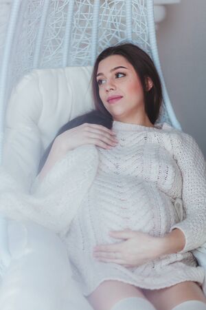 Pregnant woman holds her belly. Wears white knitted sweater. White effect photoの写真素材