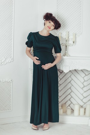 Beautiful pregnant woman in a black dress on a background of the fireplace with candles in white roomの写真素材