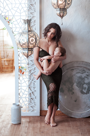 Young brunette woman breastfeeding baby standing in vintage interior. Studio shotの写真素材