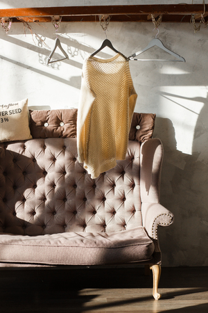Fashionable pullover hanging on rack at modern dressing room with sofa. Hard shadowsの写真素材