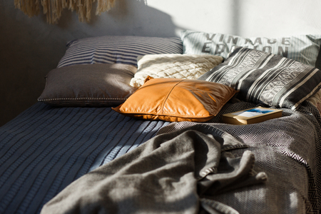 Gray bed, colored pillows and textured wall in the background. Close-up shot, focus on leather pillowの写真素材