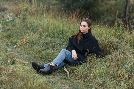 Brunette woman lying on dark green autumn grass. Casual fashion styleの写真素材