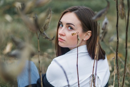 Portrait of a woman in white shirt, sitting with the back to the camera, looking back. Autumn forestの写真素材