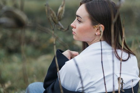 Portrait of a woman in white shirt, sitting with the back to the camera, looking leftside. Autumn forestの写真素材
