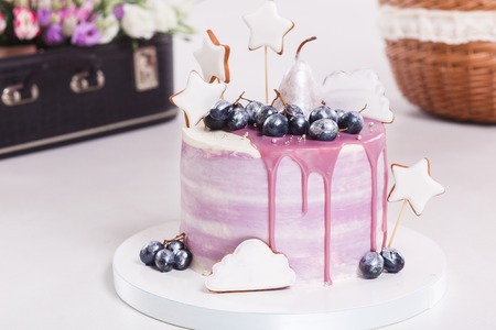 Round mousse cake decorated with grapes and pear in purple glaze and whipped cream on white cake board and table, side view.の写真素材