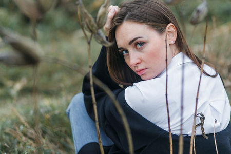 Portrait of a woman in white shirt, sitting with the back to the camera, looking back. Autumn forestの写真素材