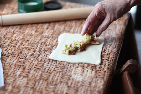 Turnovers with apple. Baker is putting apple pieces on puff pastry dough before baking.の写真素材