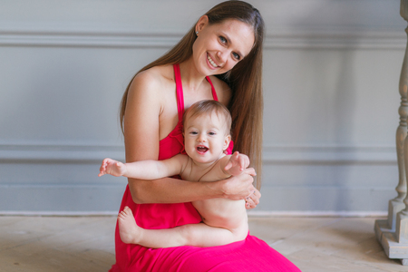 Young mother hugging happy smiling baby sitting on floorの写真素材